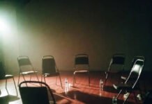 The Importance of LGBTQ+ Community in Times of Crisis Empty support circle chairs in dim basement, exhausted POV