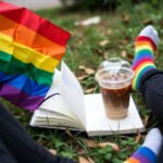 How to Find Your LGBTQ+ Community: 7 Ways to Connect with Like-Minded People First-person view of pride flag, notebook, iced coffee, and rainbow socks on grass.
