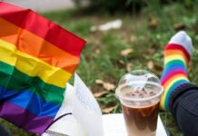 How to Find Your LGBTQ+ Community: 7 Ways to Connect with Like-Minded People First-person view of pride flag, notebook, iced coffee, and rainbow socks on grass.